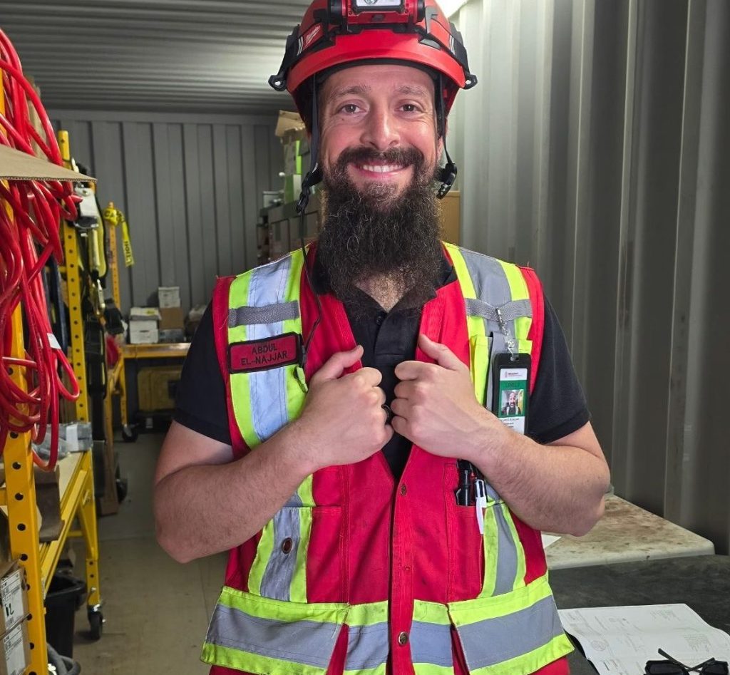Abdul in his electrical work attire looking at the camera smiling proudly.