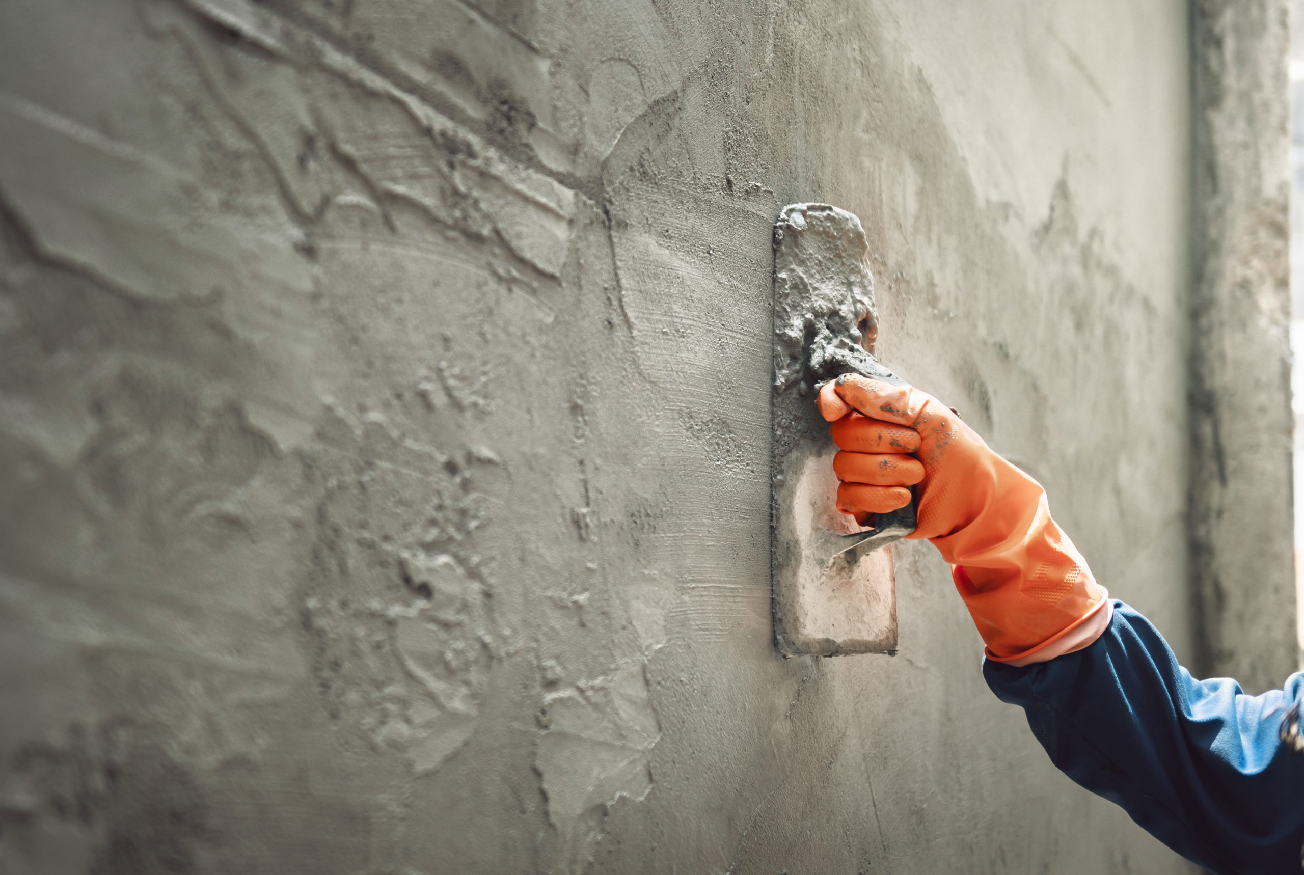 An image of a worker's hand plastering cement at a wall for building a house.